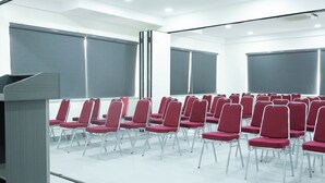 Une salle de conférence avec des rangées de chaises rouges, un pupitre et de grandes fenêtres.