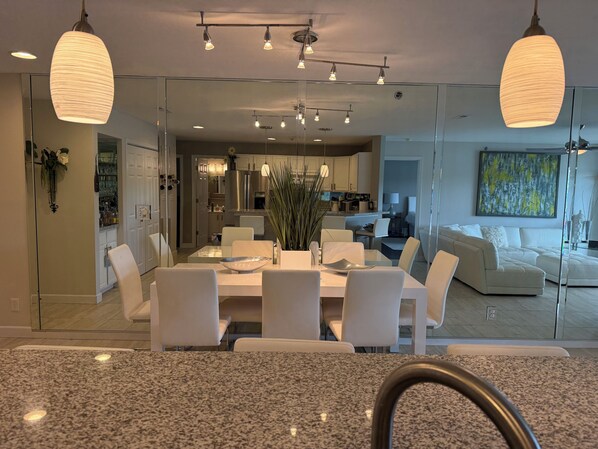 A modern kitchen with white cabinets, a stainless steel refrigerator, and a dining area with a white table and chairs.