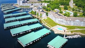 An aerial view of a waterfront hotel with multiple docked boats, a large building with a swimming pool, and lush greenery surrounding the area.