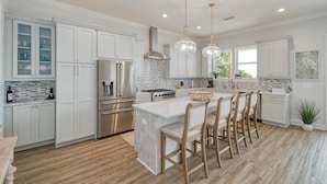 A modern kitchen with white cabinetry, a central island with bar stools, stainless steel appliances, and pendant lighting.