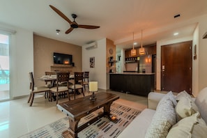 A modern living room with a dining area, a kitchen, and a large wooden door.