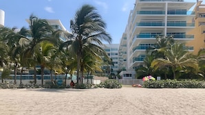 Een zandstrand met palmbomen en een modern gebouw op de achtergrond.