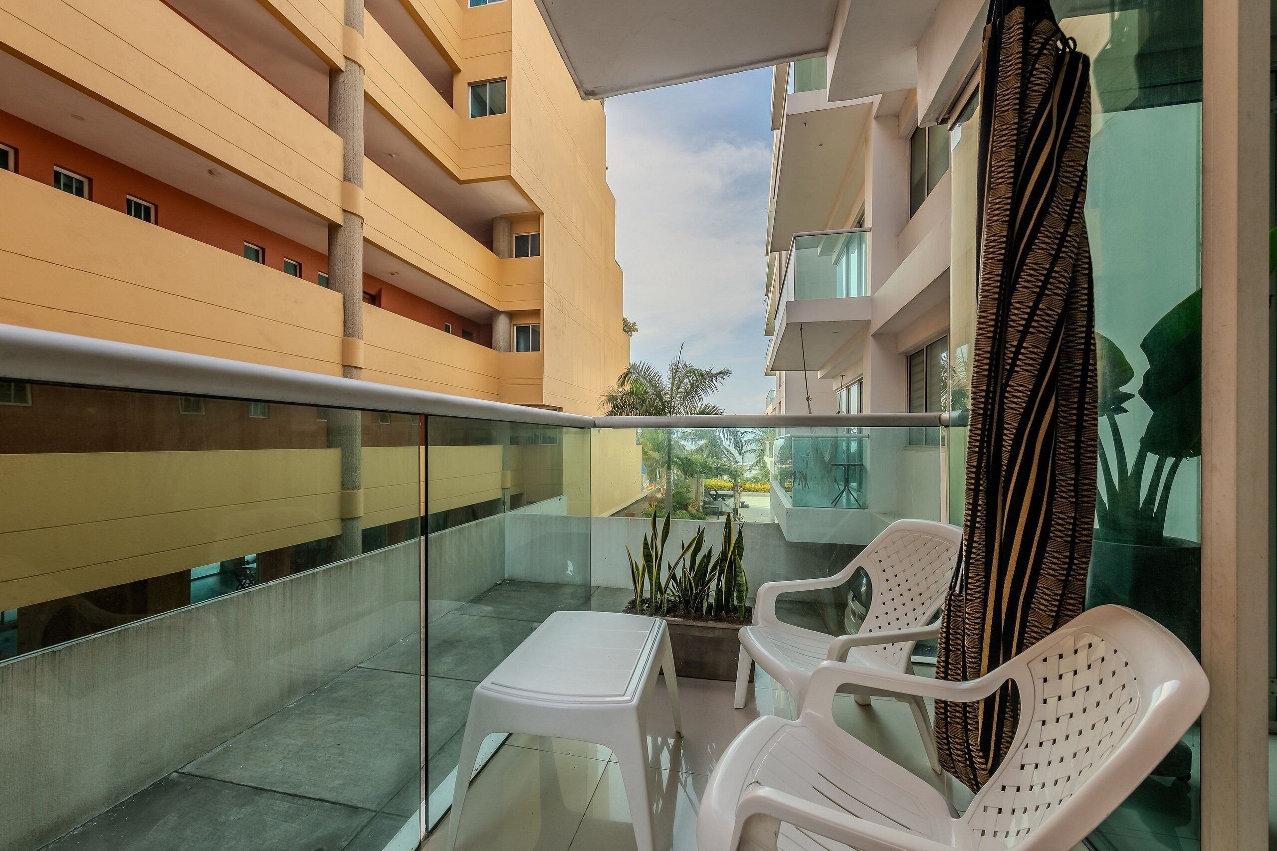 Un balcon avec des chaises en plastique blanches, une petite table et un pot de fleurs.