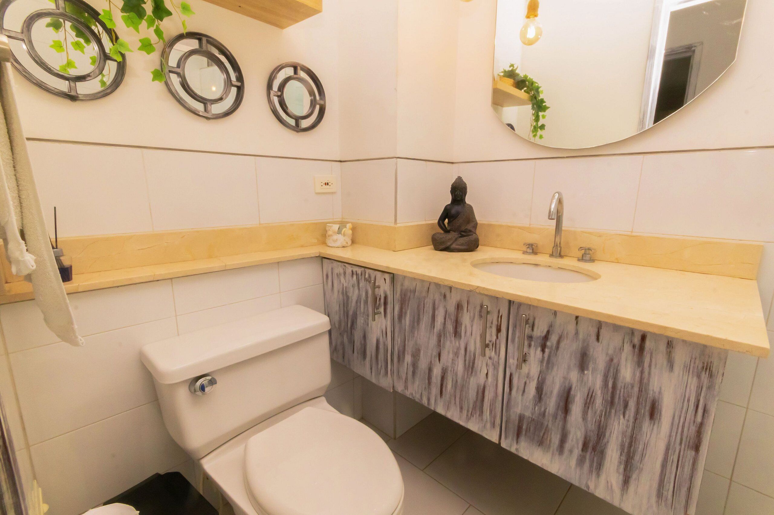 A bathroom with a toilet, sink, and mirror. There are decorative plates on the wall and a small statue on the sink.
