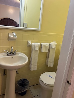 A bathroom with a white sink, a toilet, and a mirror above the sink. There are towels hanging on a rack and a trash bin under the sink.