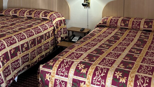 A hotel room with two beds, a nightstand, a lamp, and two framed floral artworks on the walls. - Bedford Motel  (Bedford)