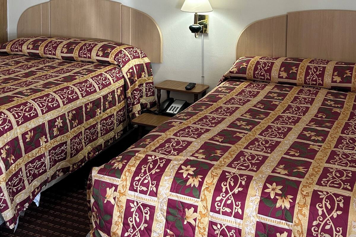 Ein Hotelzimmer mit zwei Betten, einem Nachttisch, einer Lampe und zwei gerahmten Blumenbildern an den Wänden.