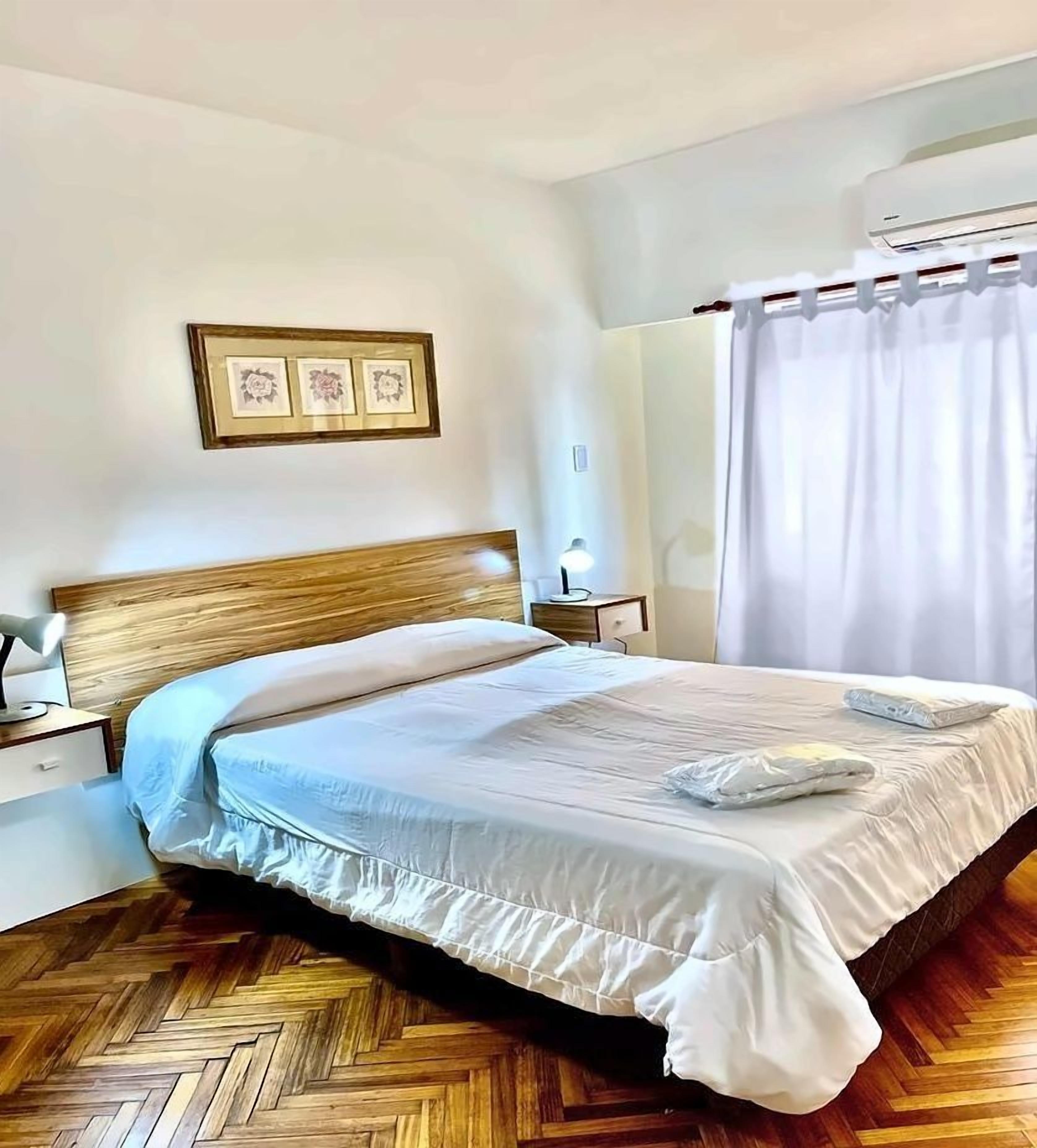 A neatly made bed with a wooden headboard, a bedside table with a lamp, and a framed picture on the wall.