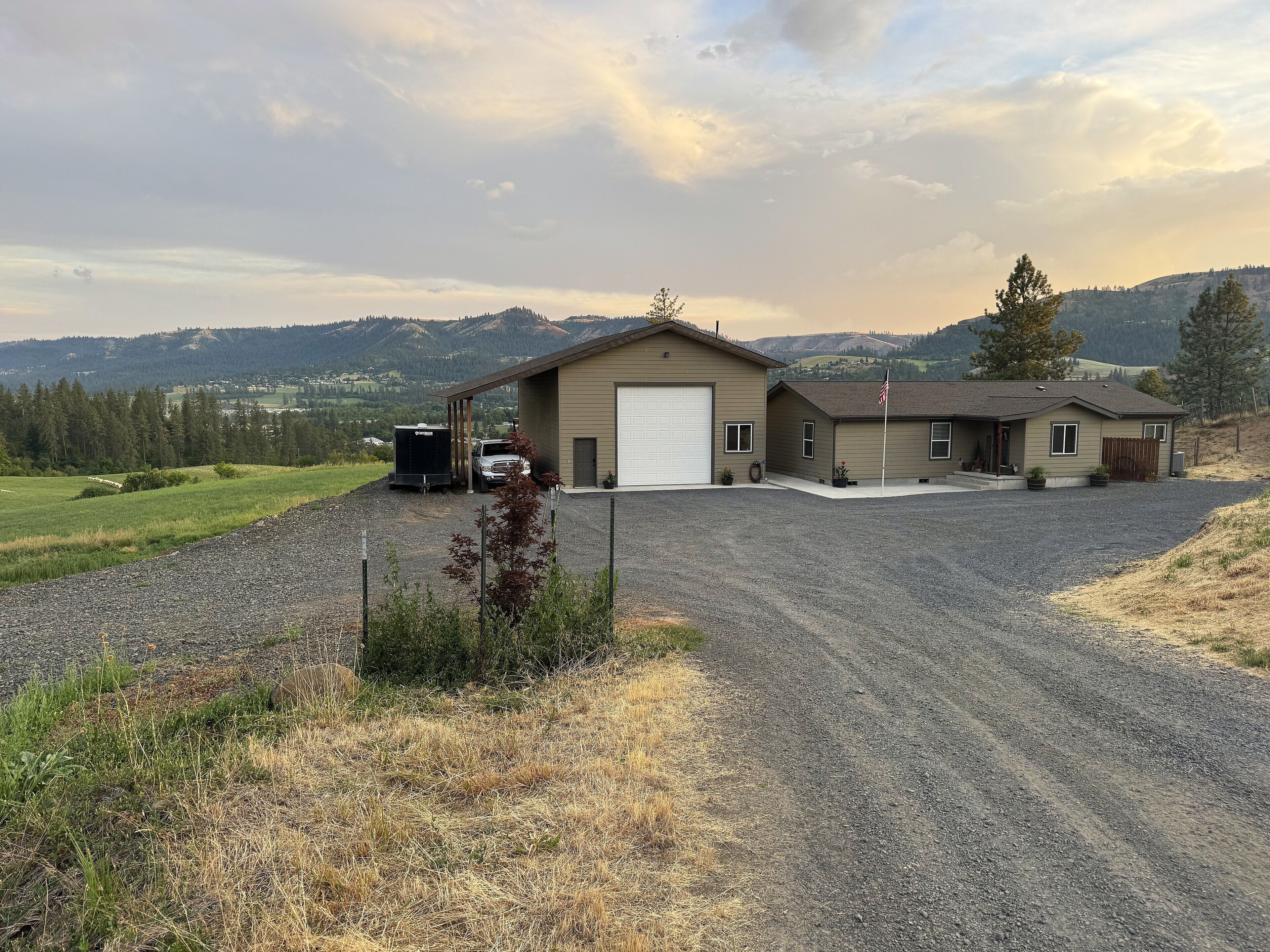 A two-story building with a garage, a covered driveway, and a gravel parking area.