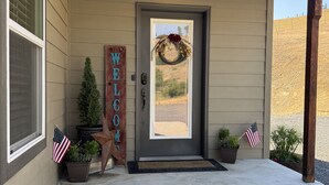 A house entrance with a welcome sign, a wreath on the door, American flags, and potted plants. - 4BR Ranch Retreat w/Hot Tub & Senic Valley Views + Mini House Add-On (Kamiah)