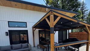 A covered outdoor seating area with a wooden bench, a table, and a sofa. - House in tranquil Tamworth NH with AC, Hot Tub, Riverfront access (Tamworth)