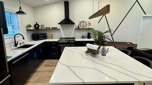 A modern kitchen with a large island, black cabinets, and a white marble countertop. - House in tranquil Tamworth NH with AC, Hot Tub, Riverfront access (Tamworth)