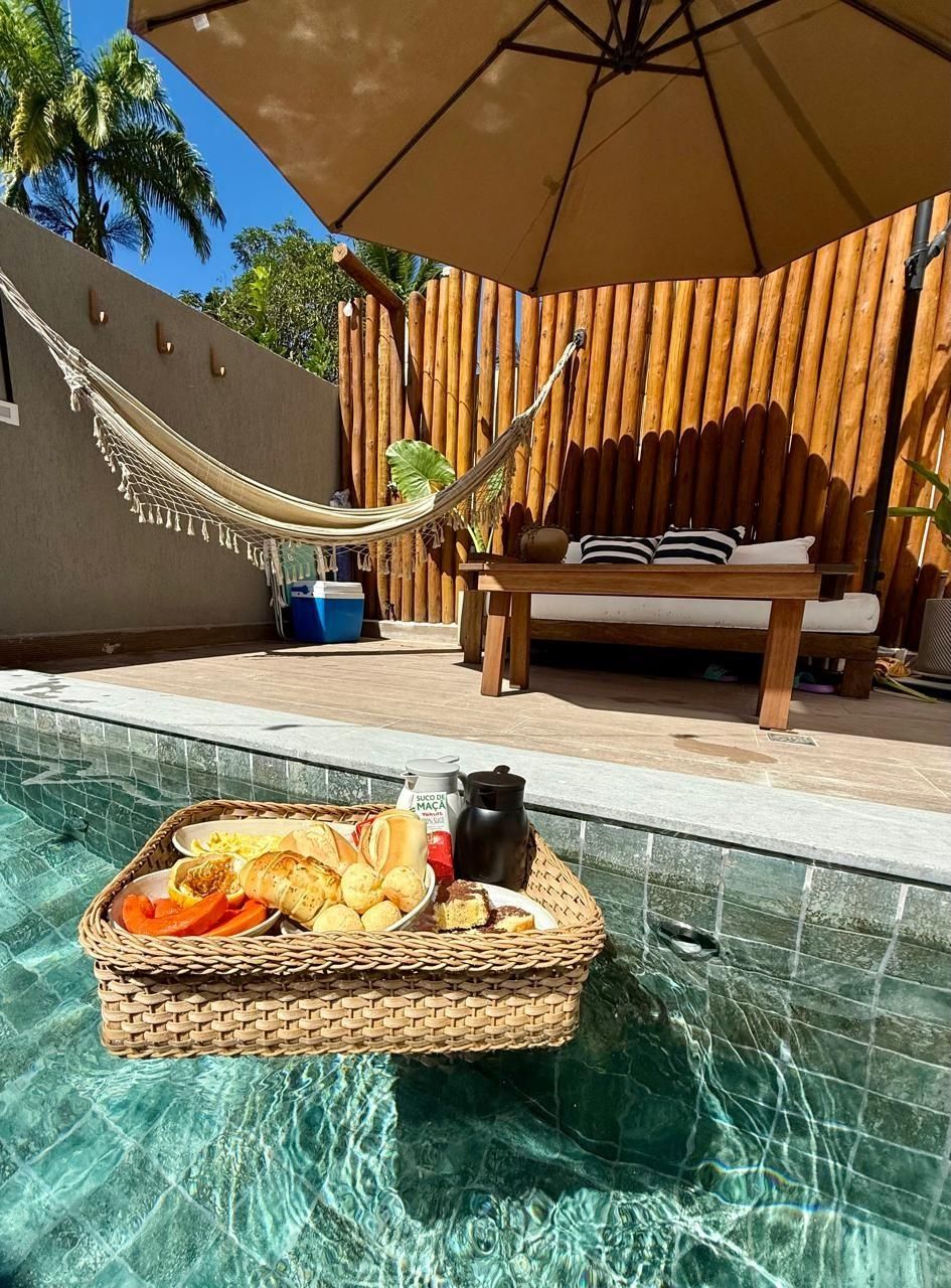 A poolside area with a wicker basket of food, a hammock, and a wooden bench under an umbrella.