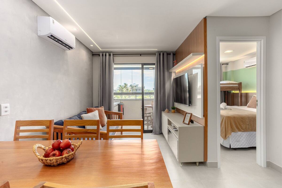 A modern living room with a dining table, chairs, a TV, and a balcony with a view.
