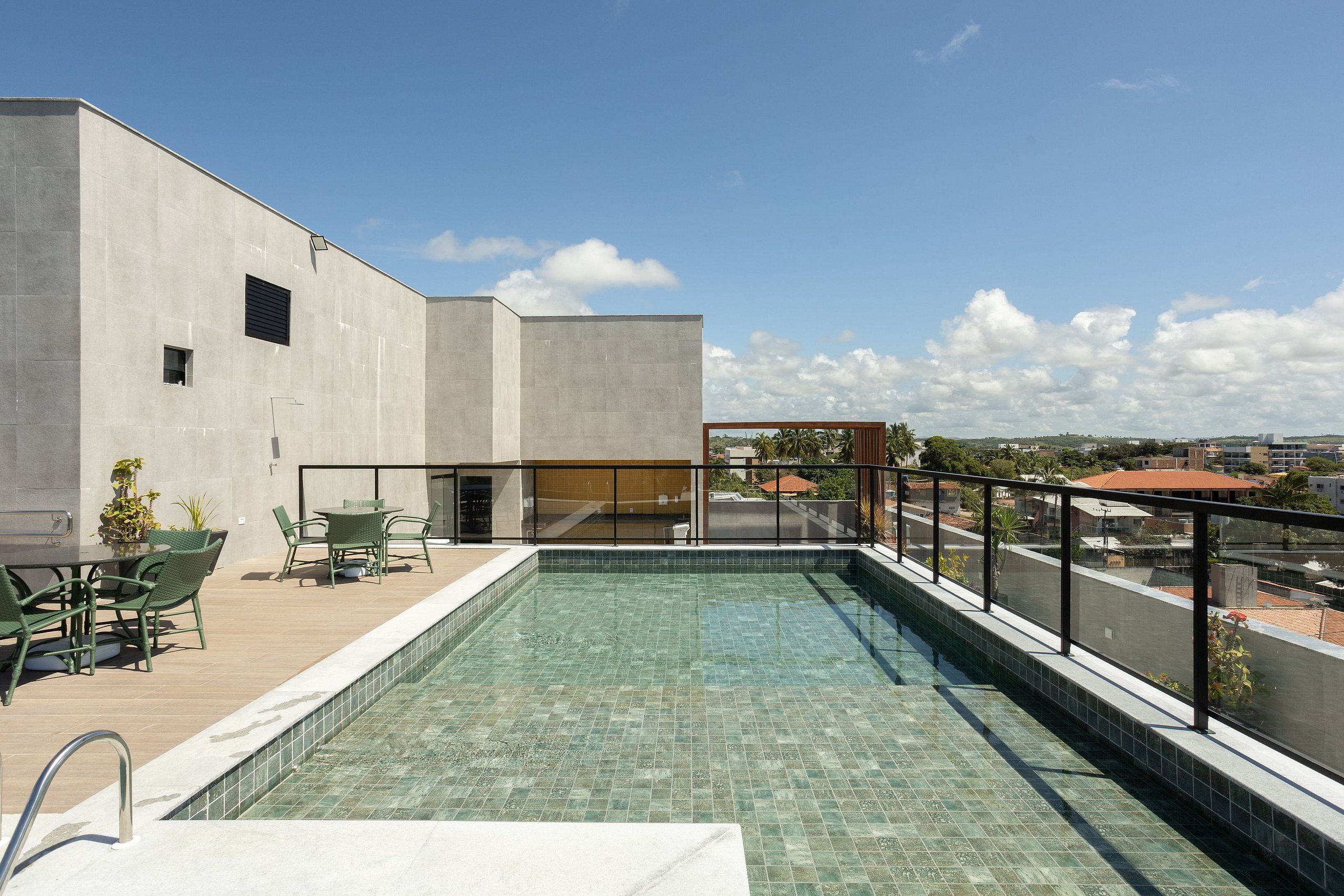 Una piscina en la azotea con vistas despejadas de la ciudad, un área de descanso con sillas y una fachada de edificio moderna.