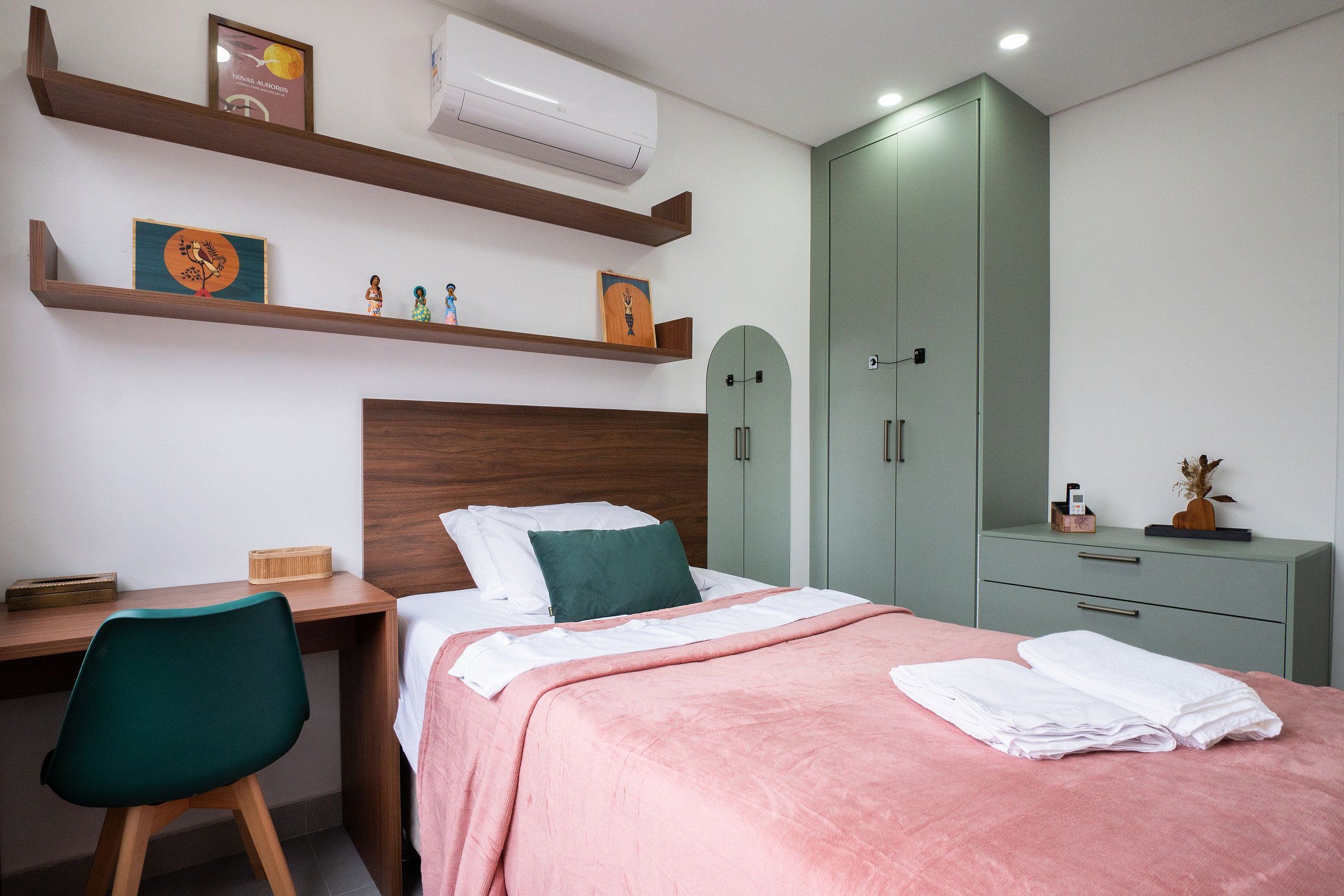 Un dormitorio con cama, escritorio, silla, armario y estanterías con objetos.