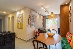 A modern kitchen with a gas stove, a dining area with a round table and chairs, a green sofa, and a large window with a view of the outdoors. - Edf Tours du Porto - Centro (Ipojuca)