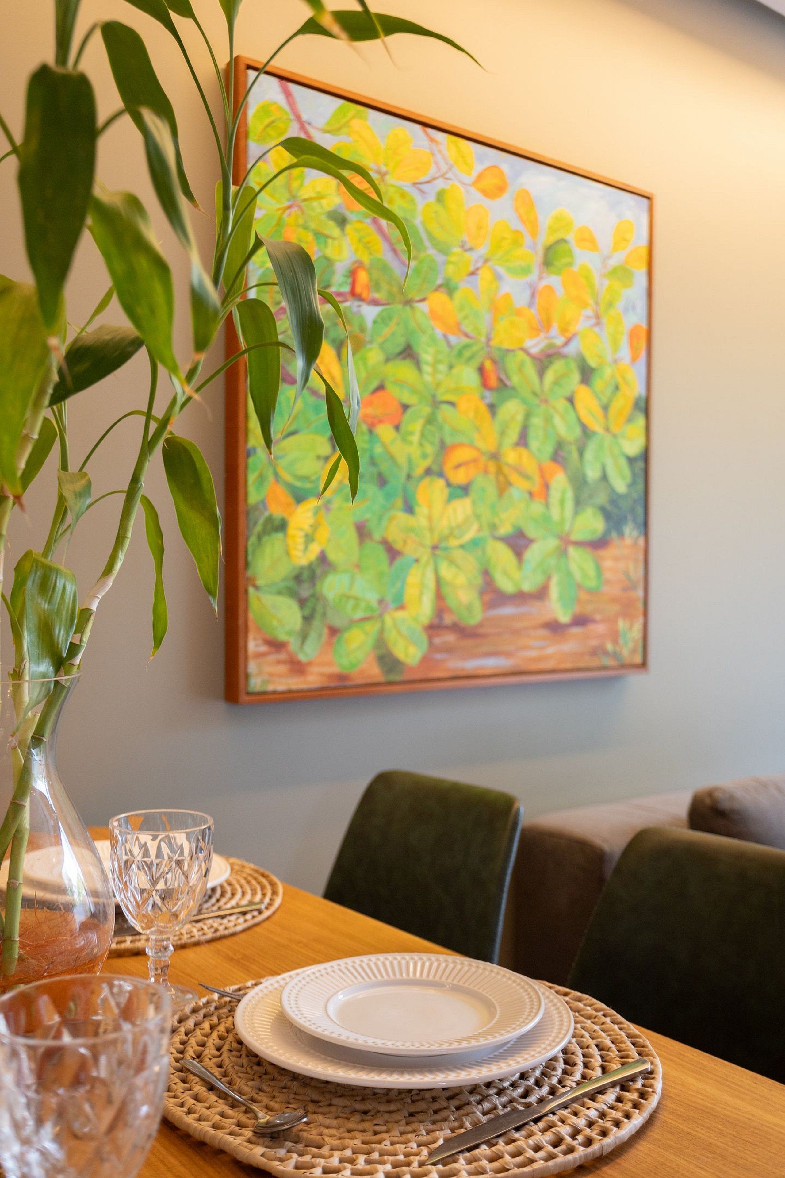 A dining table with a vase of green leaves, a glass, and a plate set for two.