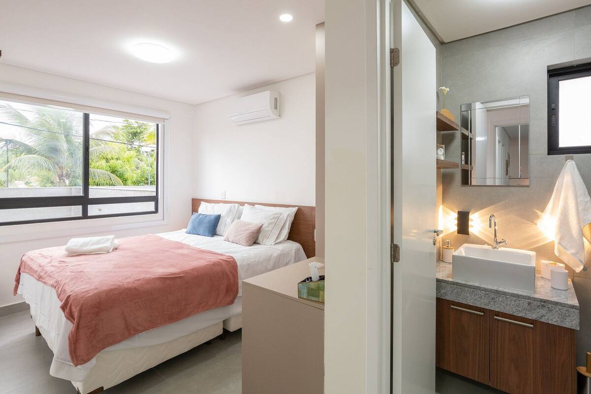 A bedroom with a bed, a window, and a bathroom with a sink and mirror.