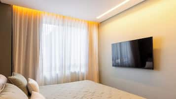 A hotel room with a bed, a TV mounted on the wall, and a large window with curtains.