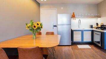 A modern kitchen with a refrigerator, sink, and cabinets. There is a dining table with chairs and a vase of sunflowers.