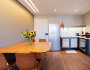 A modern kitchen with a refrigerator, sink, and cabinets. There is a dining table with chairs and a vase of sunflowers. - Edf Tours du Porto - Centro (Ipojuca)