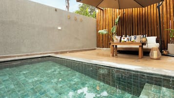 Une piscine à l’eau claire, une terrasse en bois, un canapé et une table avec des boissons.