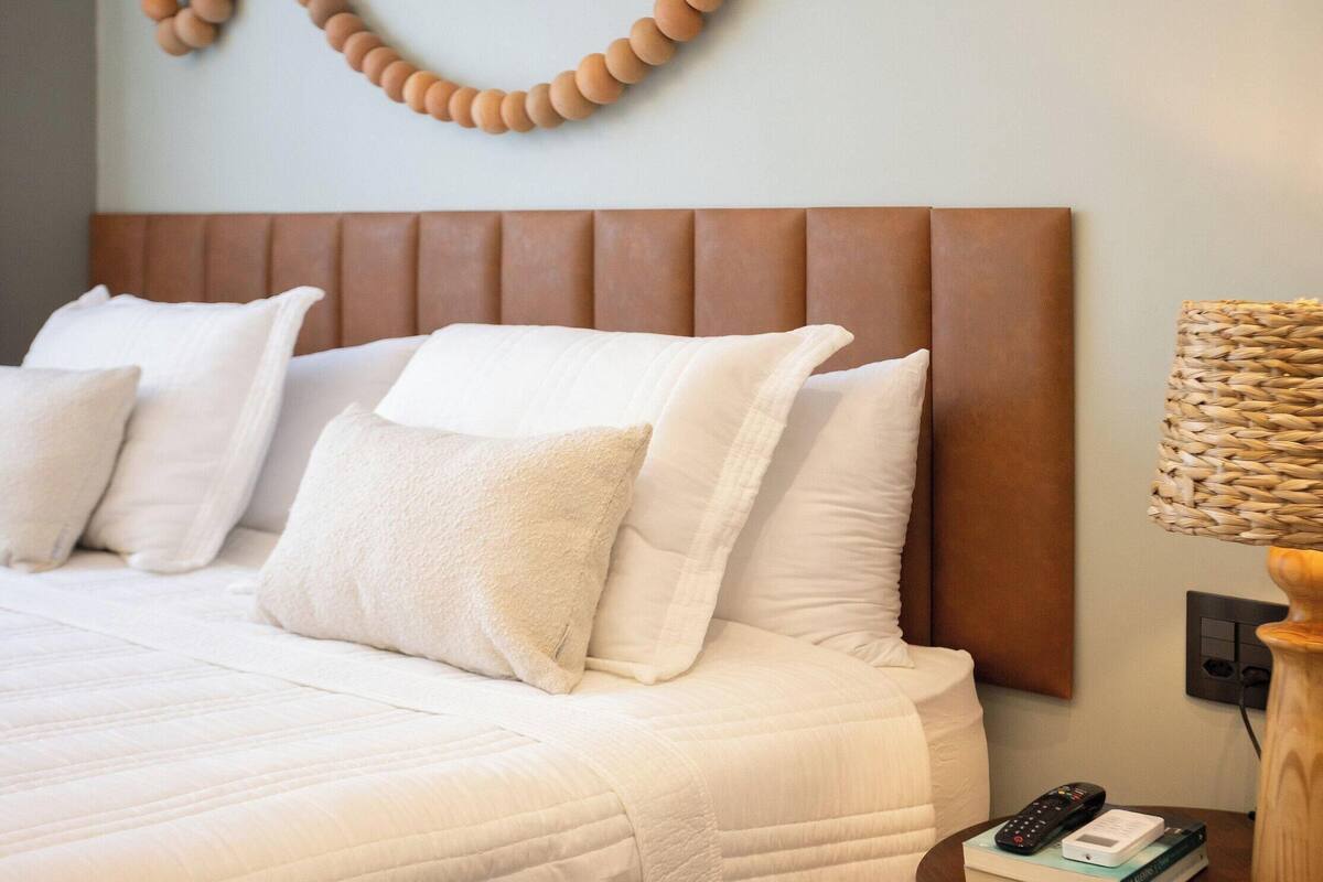 A neatly made bed with white bedding, a wooden headboard, and a wall-mounted decorative item.