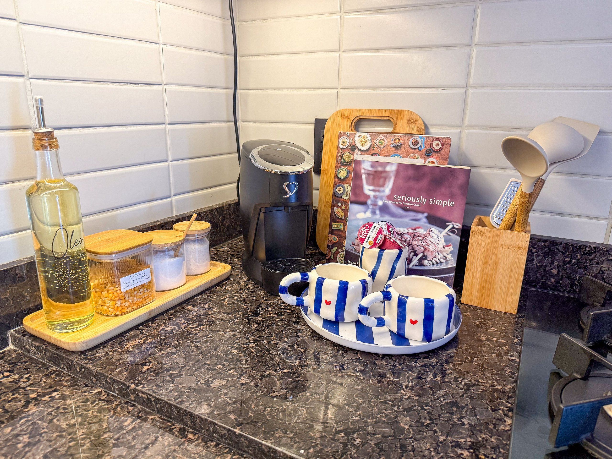 A kitchen counter with a coffee maker, a bottle of oil, jars of spices, a cookbook, and kitchen utensils.