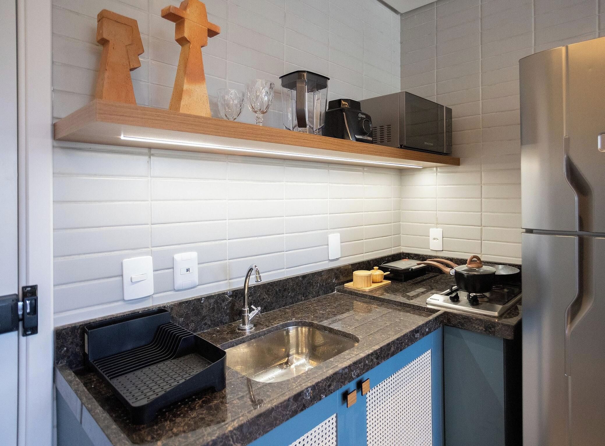 Una cocina con un refrigerador de acero inoxidable, un lavamanos con grifo, un microondas y un estante con adornos.