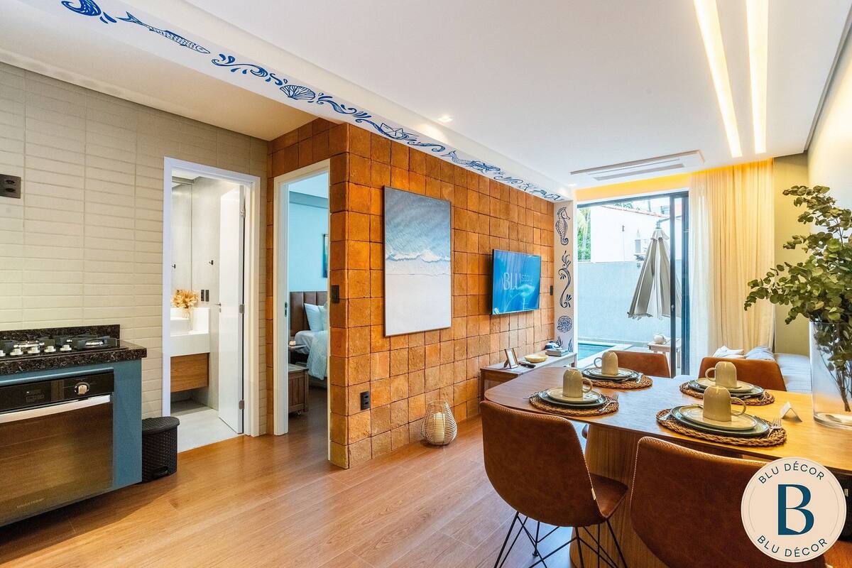 A modern kitchen with a built-in stove, a dining area with a wooden table set for four, and a view of the sea through a large window.