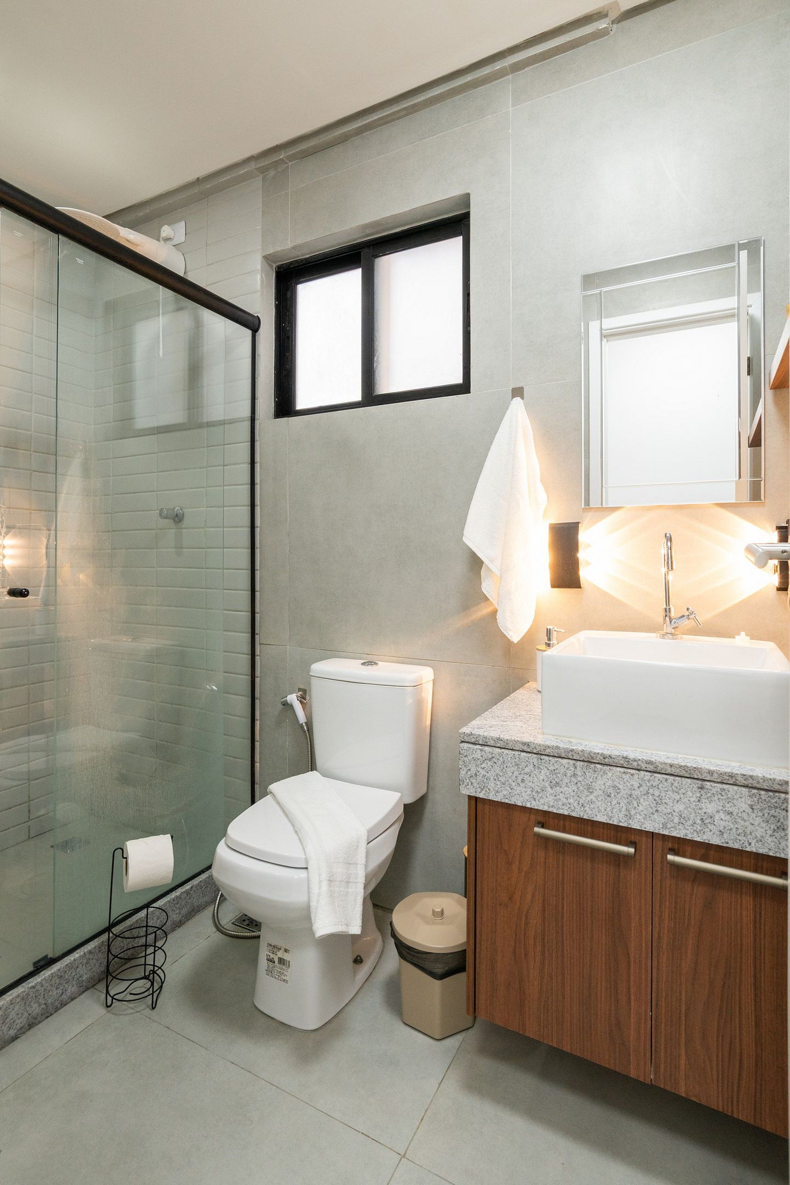 A modern bathroom with a glass shower enclosure, a toilet, a sink with a mirror, and a towel rack.