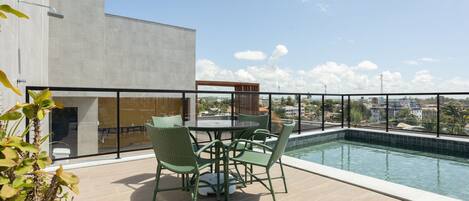 A rooftop pool area with a table and chairs, a potted plant, and a view of the city skyline.