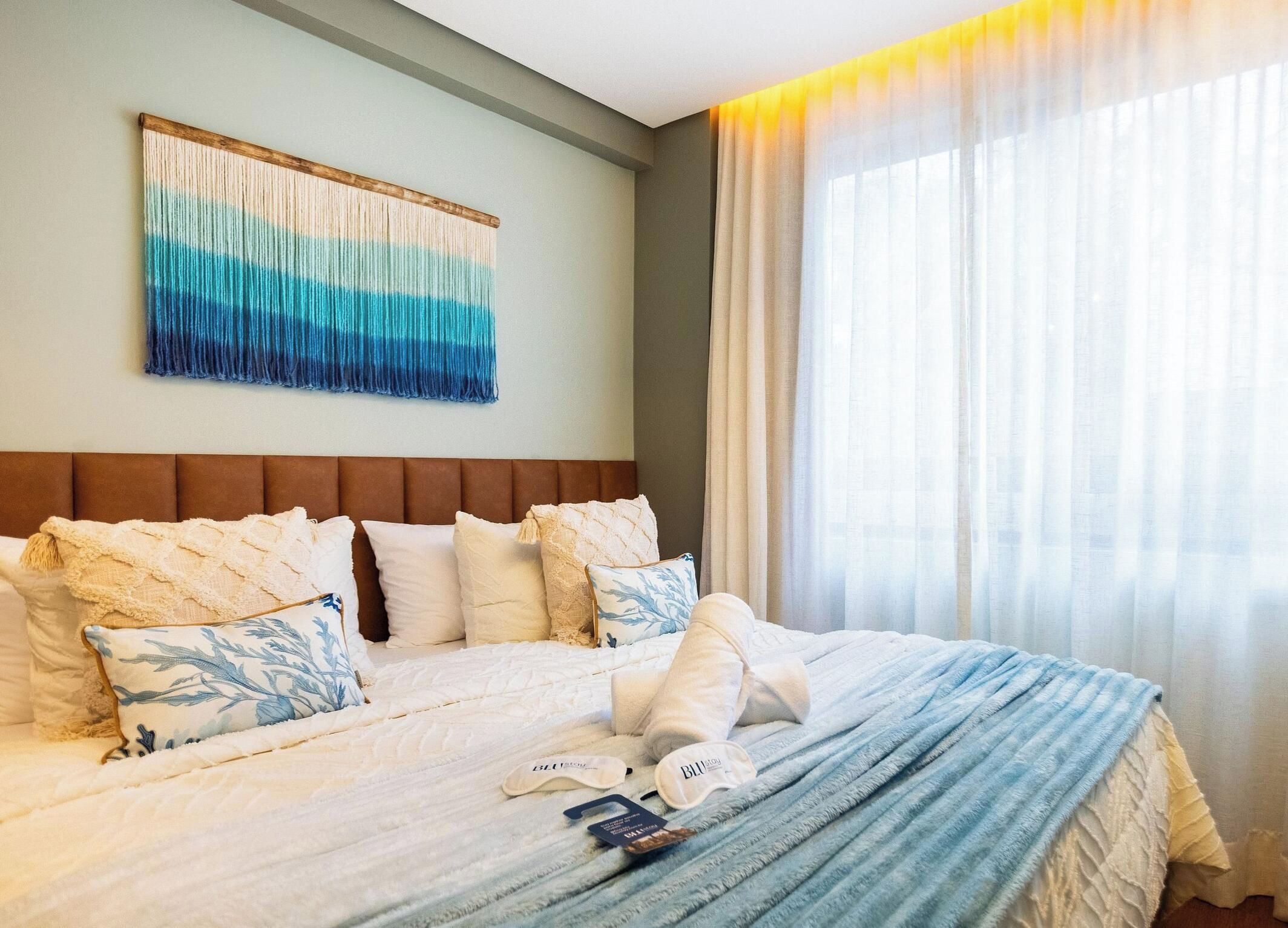 A hotel room with a large bed, a headboard, and a window with curtains.