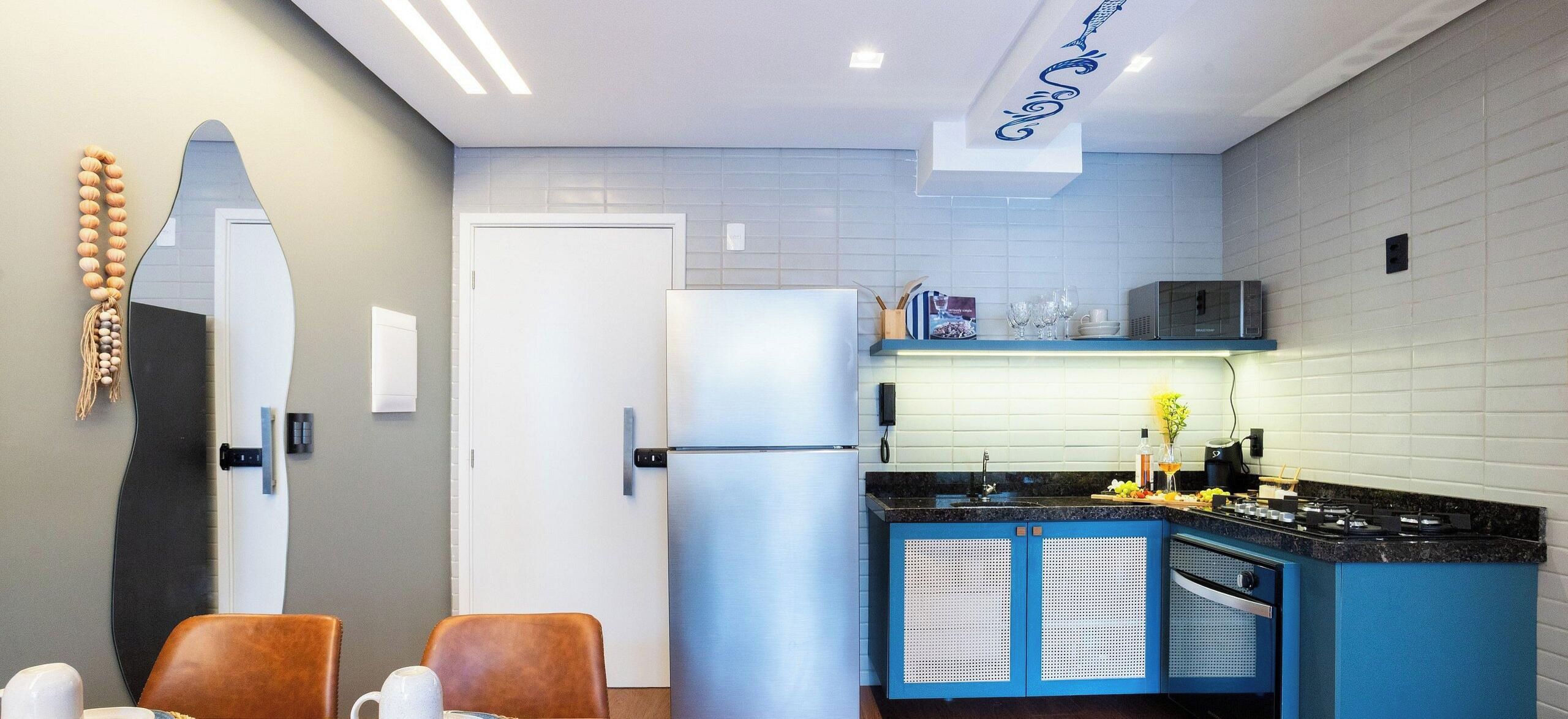A modern kitchen with a refrigerator, microwave, and blue cabinets. There is a dining area with two chairs and a table.