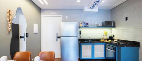 A modern kitchen with a refrigerator, microwave, and blue cabinets. There is a dining area with two chairs and a table.