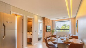 Une cuisine moderne dotée d’un réfrigérateur en acier inoxydable, d’un coin repas avec une table ronde et des chaises, et d’un téléviseur fixé au mur.