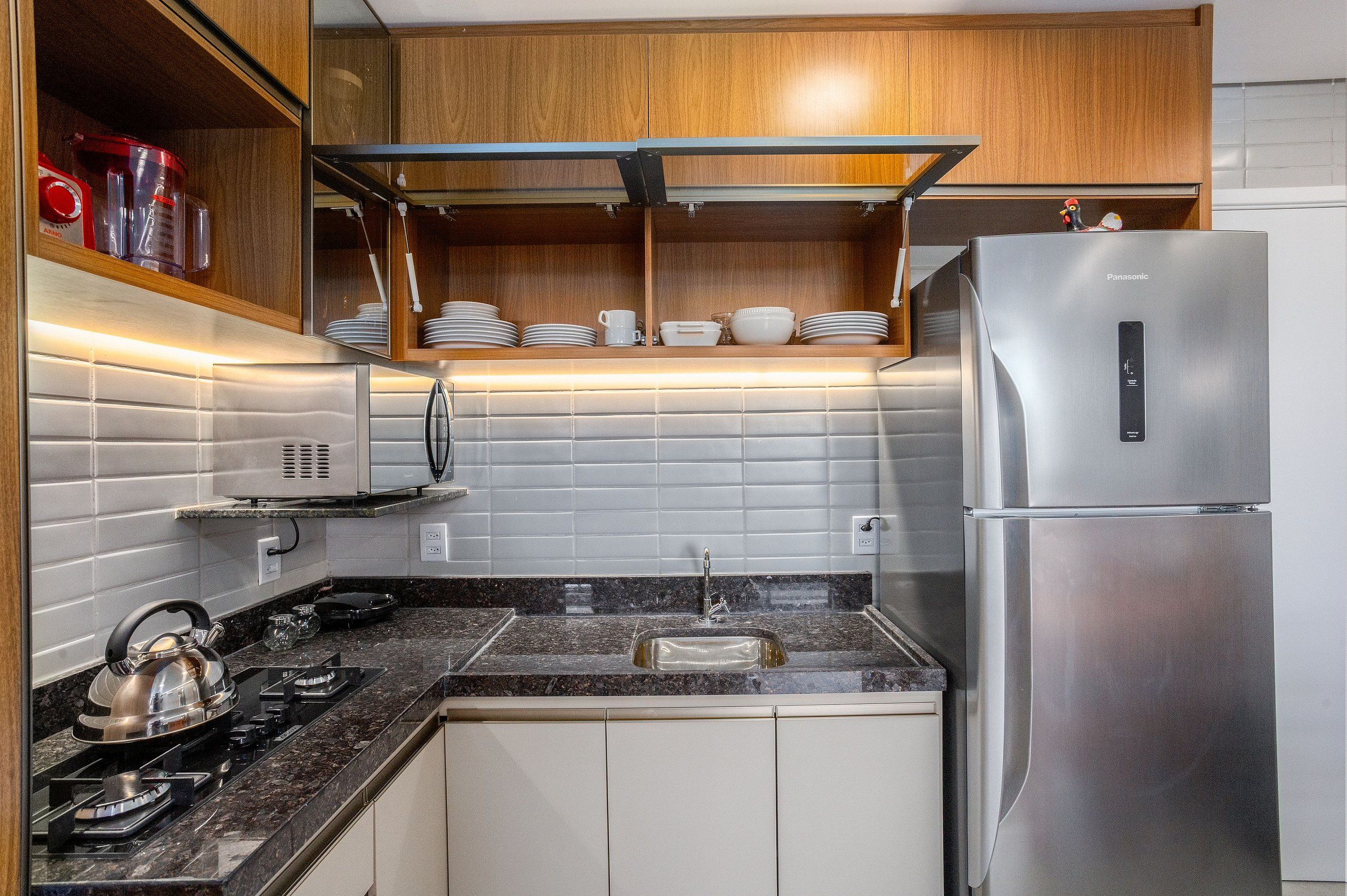 A kitchen with a stainless steel refrigerator, a gas stove, a sink, and wooden cabinets.