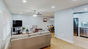 A modern living room with a sofa, TV, ceiling fan, and dining area.
