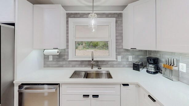 A modern kitchen with white cabinets, a stainless steel sink, a window with a view, and a coffee maker.