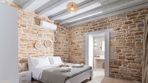 A bedroom with a stone wall, a bed, a bedside table, and a hanging light fixture.