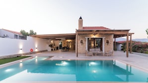 A modern house with a swimming pool, a covered patio, and a stone chimney.