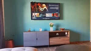 Een woonkamer met een flatscreen-tv aan de muur, waarop de film 'Brightburn' draait. Er staat een grijze kast met decoratieve spullen erop en een kleine plant ernaast.