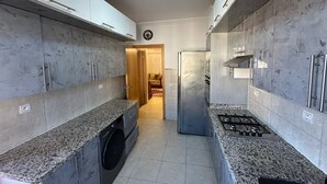 Een moderne keuken met granieten aanrechtbladen, roestvrijstalen apparatuur en een ingebouwde wasmachine.