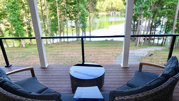 A covered outdoor seating area with wicker furniture and a table, overlooking a lake and trees. - Forget Me Not Haven – 6BR Lakefront Home for Unforgettable Family Memories (Speedwell)