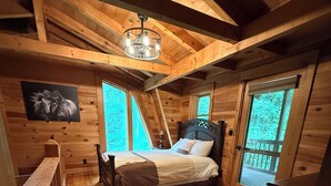 Camera da letto di una baita in legno con un letto, una panca in legno, un tappeto e un quadro appeso al muro.