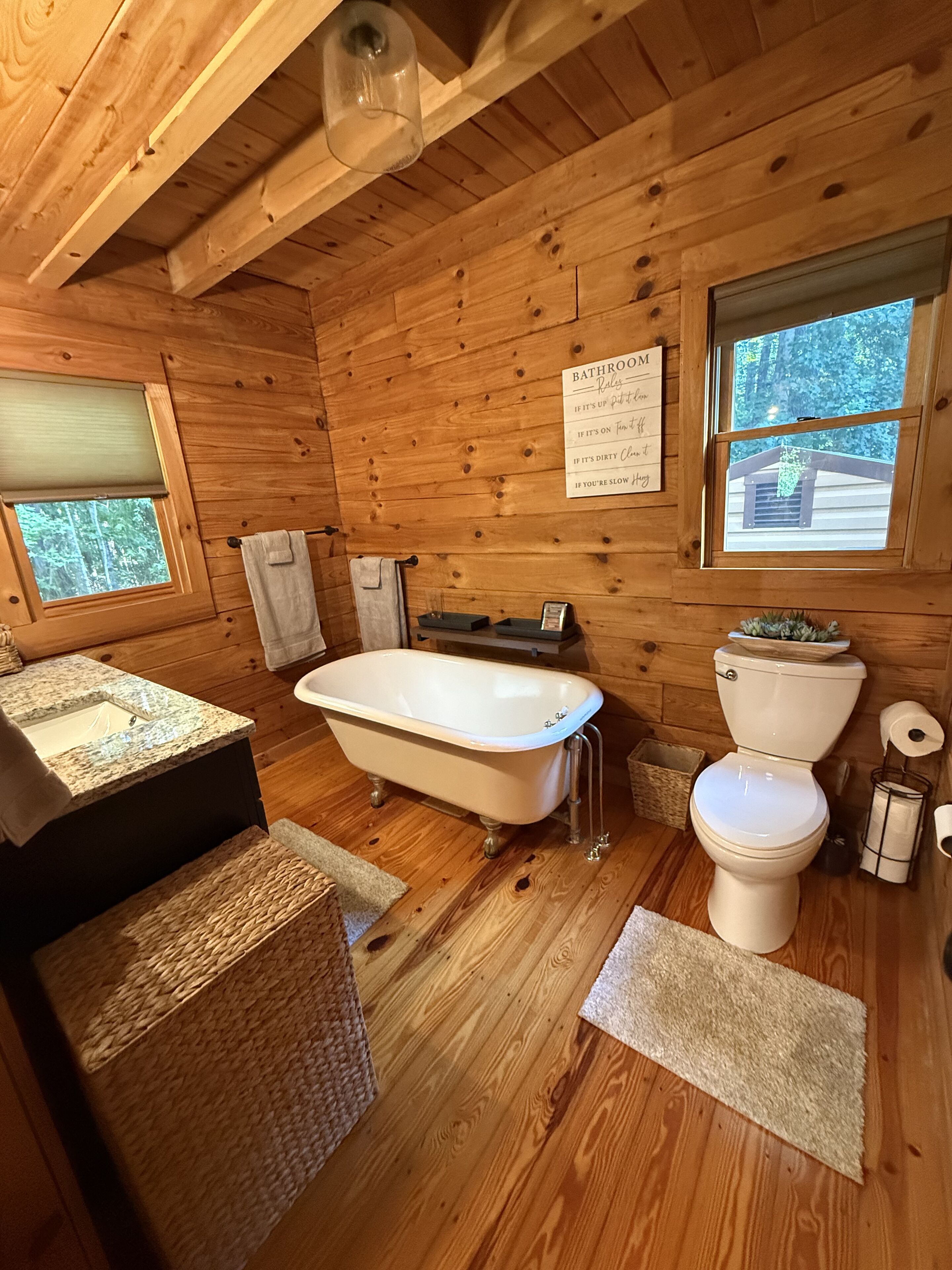 Une salle de bain rustique, avec des murs en bois, comprenant une baignoire sur pieds, des toilettes et un lavabo.