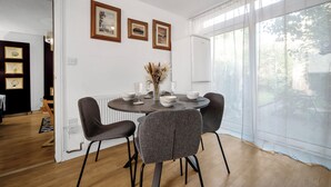 Un comedor con una mesa redonda, cuatro sillas grises y un florero con flores secas. Hay tres cuadros enmarcados en la pared sobre la mesa.