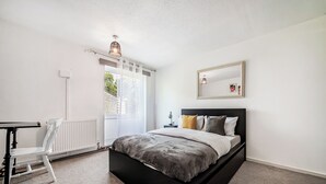 Un dormitorio con cama, una silla, un radiador, una ventana y un espejo en la pared.