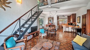 Amplia sala de estar con una escalera de madera, una mesa de comedor y una cocina al fondo.